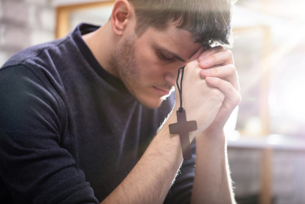 Depositphotos_267549916_XL Side View Of Religious Young Man With Rosary Praying To God At Home